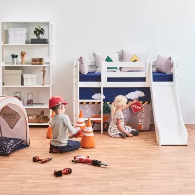 Cama infantil branca com escorrega, almofadas coloridas, crianças a brincar com cones de trânsito e ferramentas, estante branca e tenda de tecido