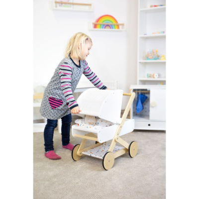 Menina a empurrar carrinho de bonecas branco com estofos coloridos em quarto infantil