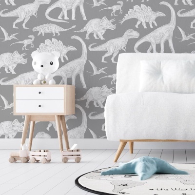 Quarto infantil com papel de parede de dinossauros brancos em fundo cinzento, móvel de madeira clara com figura de urso, carrinho de madeira, sofá branco e tapete com brinquedo azul.