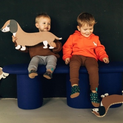 Duas crianças sentadas num banco azul com figuras de cães de cartão