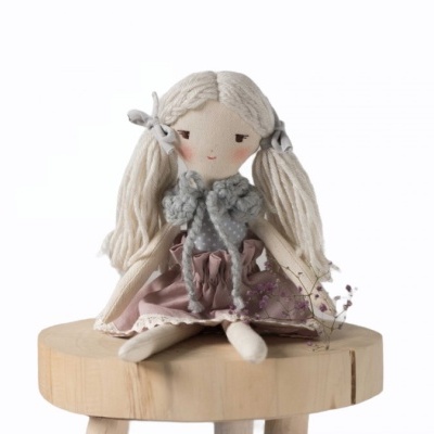 Boneca de pano loira com vestido rosa sentada numa cadeira de madeira clara