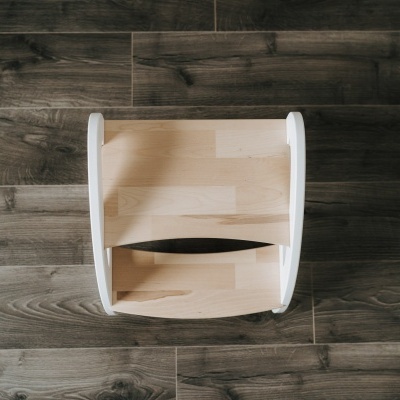 Cadeira em madeira clara com dois degraus e laterais brancas sobre chão de madeira castanha escura