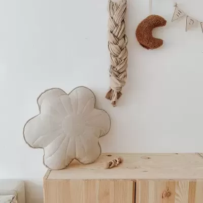 Almofada em forma de flor cinza claro sobre móvel de madeira, decoração de parede com peça trançada e forma de lua castanha