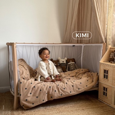 Cama de criança com roupa de cama bege com pontos pretos e peluches em quarto com decoração neutra.