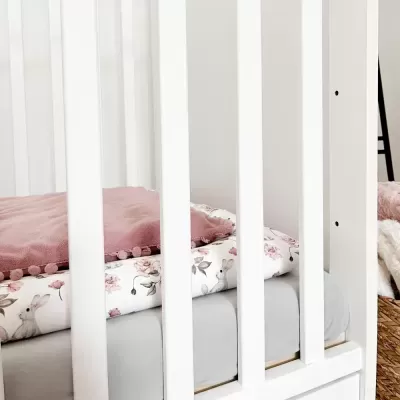 Berço branco com roupa de cama rosa e padrão de coelhos.
