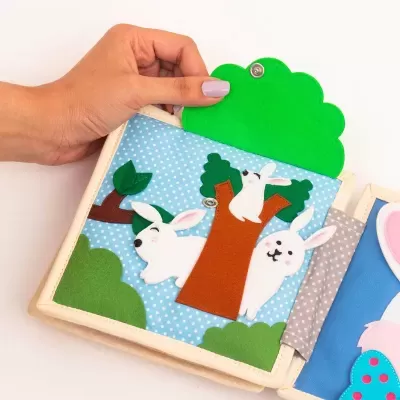 Livro infantil de tecido com coelhos e árvore em fundo azul com bolinhas brancas