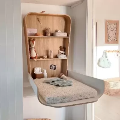 Muda fraldas dobrável branca com prateleiras em madeira clara e objetos decorativos