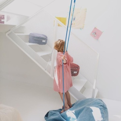 Criança em baloiço azul numa divisão branca com escada e desenhos nas paredes