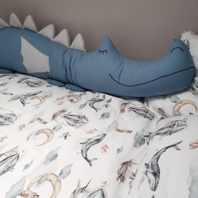 Travesseiro crocodilo azul sobre cama com lençol branco estampado náutico