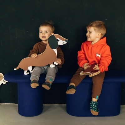 Duas crianças sentadas num banco azul segurando brinquedos de cartão em forma de cães.