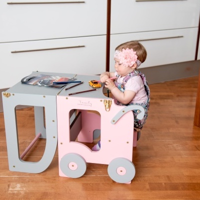 Criança sentada num carrinho de brincar rosa e cinza dentro de casa
