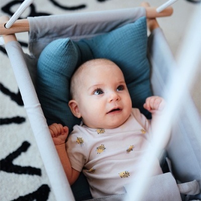 bebé deitado em rede suspensa cinza com almofada azul, body branco com abelhas amarelas, tapete branco com letras negras