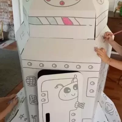 Foguete de brincar de cartão branco com desenhos a preto e rosa em ambiente interior