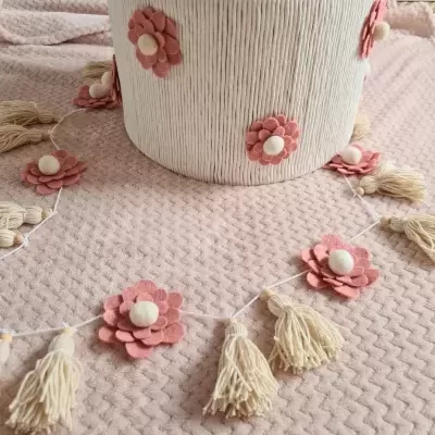 Cesta branca decorada com flores cor-de-rosa e pendente com pompons creme sobre tecido rosa