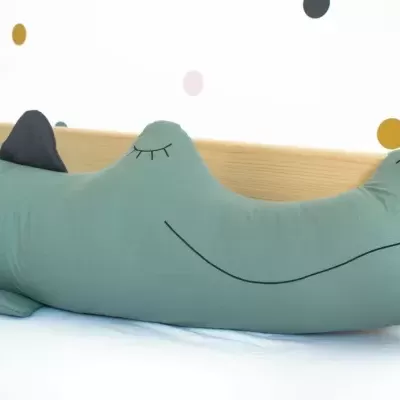 Almofada em forma de crocodilo verde com crista preta sobre cama