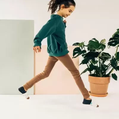 Criança a saltar com roupa casual em ambiente interior com planta e placas coloridas