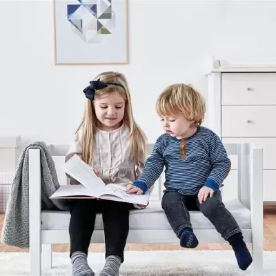 Cama infantil branca de madeira com duas crianças sentadas lendo em quarto minimalista branco.