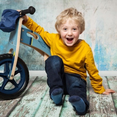 Criança com bicicleta infantil de madeira azul sentada no chão de madeira colorida