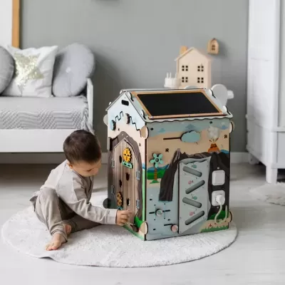 Casa de brincar de madeira colorida para crianças, com atividades nas paredes, colocada num quarto com tapete branco