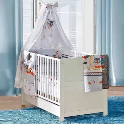 Berço branco decorado com têxteis de corujas num quarto com cortinas azuis