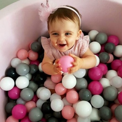Bebé numa piscina de bolas coloridas a sorrir e a segurar uma bola rosa