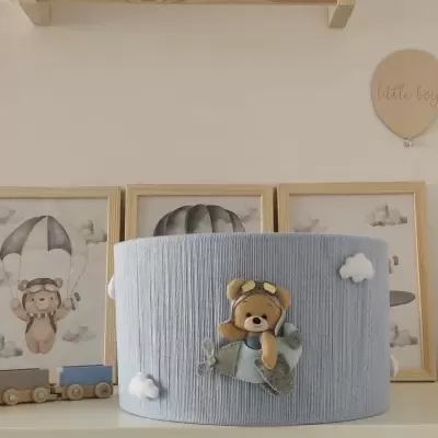 Abajur azul claro com decoração de urso aviador e nuvens em quarto infantil
