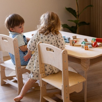 Mesa e cadeiras infantis de madeira com crianças a brincar com blocos de madeira.