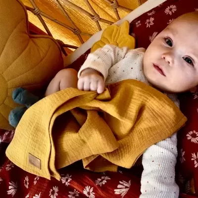 Bebé deitado com cobertor amarelo num sofá com almofadas decorativas