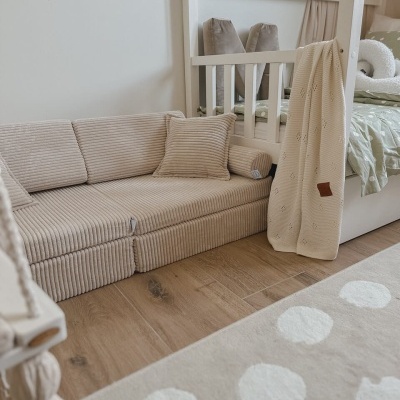 Sofá infantil bege de tecido riscado junto a cama branca com colcha verde de bolinhas e manta bege