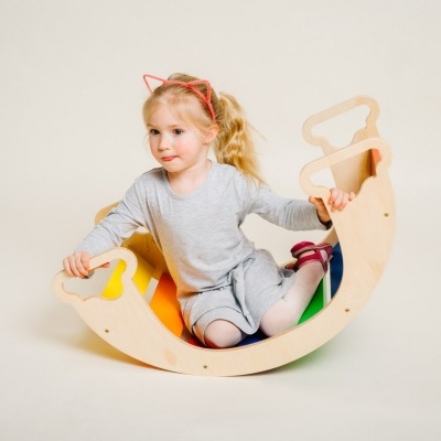 Criança com cabeçares de gato sentada num baloiço de madeira com almofadas coloridas