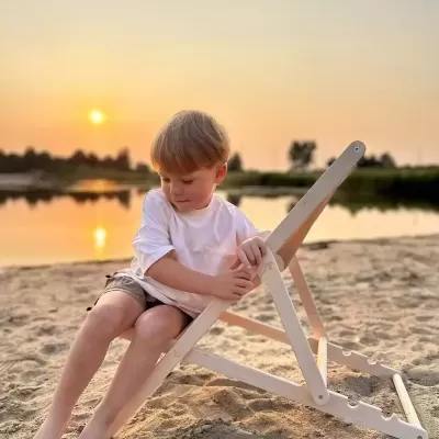 Criança numa cadeira de madeira branca ajustável na praia ao pôr do sol