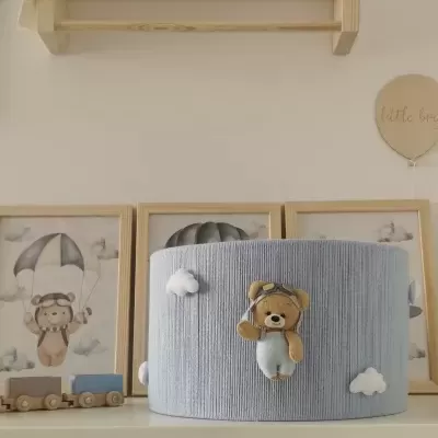 Aparelho redondo cinzento com urso aviador em tecido e nuvens brancas, em quarto infantil.