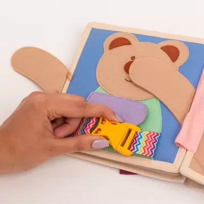 Livro de tecido infantil com urso e cinto colorido sendo manuseado