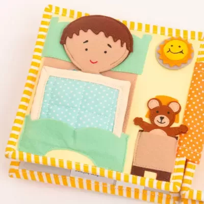 Livro infantil de tecido com menino a dormir, sol sorridente e urso pequeno