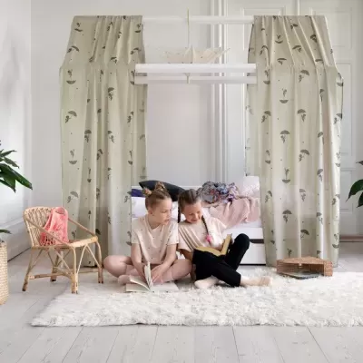 Quarto infantil com cortinas bege com padrão de guarda-chuvas, crianças a ler no tapete branco felpudo.