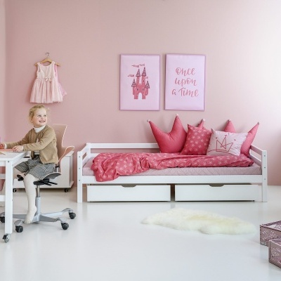 Quarto infantil rosa com cama branca, roupa de cama rosa, escrivaninha branca, cadeira de rodas e decorações cor-de-rosa.
