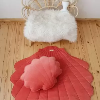 Tapete e almofada decorativos rosa em chão de madeira clara com cadeira de rattan e pelúcia branca ao fundo