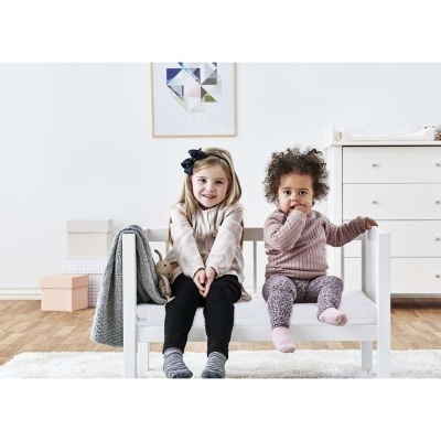 Duas crianças sentadas num sofá branco de madeira com almofada branca