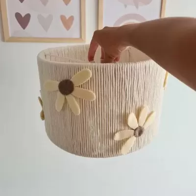 Cesto decorativo branco com flores de tecido suspenso com mão dentro e quadros de parede ao fundo