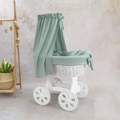 Carrinho de bebé em vime branco com forro verde claro e dossel, rodas de madeira branca, em ambiente interior