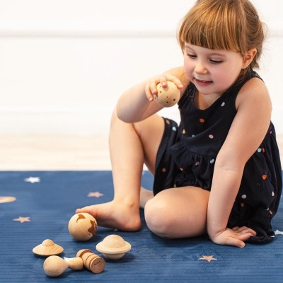 Criança a brincar com brinquedos espaciais de madeira num tapete azul com estrelas