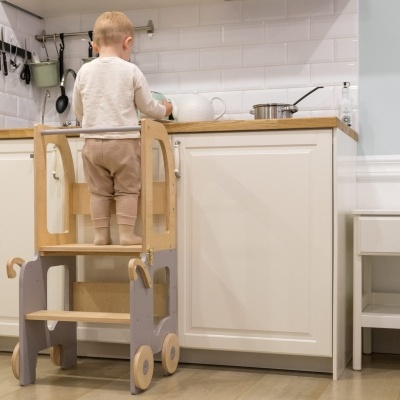 Criança em cozinha branca com banco elevatório de madeira cinza