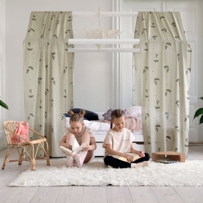 Cortinas bege com padrão de guarda-chuvas e crianças a ler em manta branca