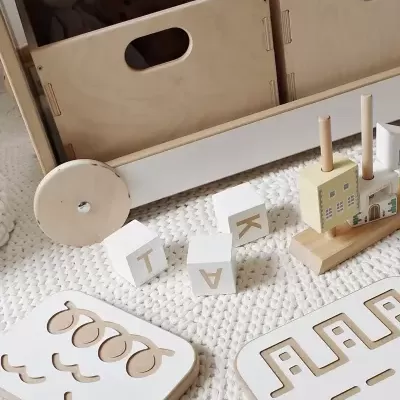 Caixa de arrumação em madeira clara com rodas e brinquedos de madeira sobre tapete branco