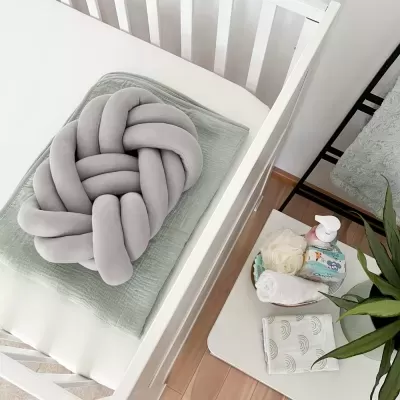 Almofada trançada cinza sobre cama branca com cobertor verde claro e mesa com itens de higiene