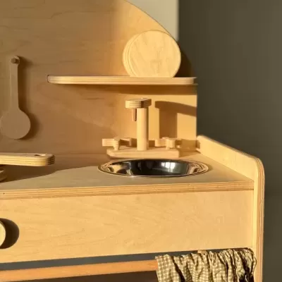 Cozinha de brincar em madeira clara com pia metálica e pano xadrez castanho