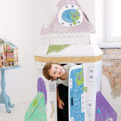 Menino sorridente dentro de foguete de papelão pintado à mão com desenhos coloridos