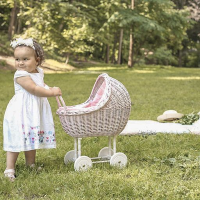 Criança de vestido branco a empurrar carrinho de bonecas em relvado