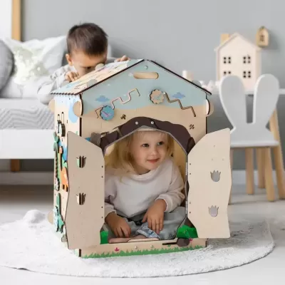 Criança dentro de casinha de brinquedo de madeira com portas abertas e decoração colorida