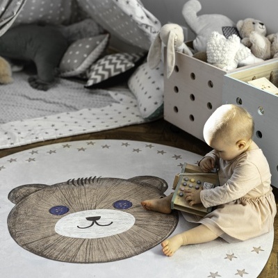 Criança sentada num tapete redondo com desenho de urso e estrelas, brincando com brinquedo de madeira, ao lado de caixa de brinquedos e tenda cinzenta com estrelas.
